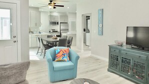 A modern living room with a sofa, a television, and a cabinet. There is a dining area with a table and chairs, and a kitchen in the background. - New Beach & Bay Retreat Full of Amenities! (Long Beach)