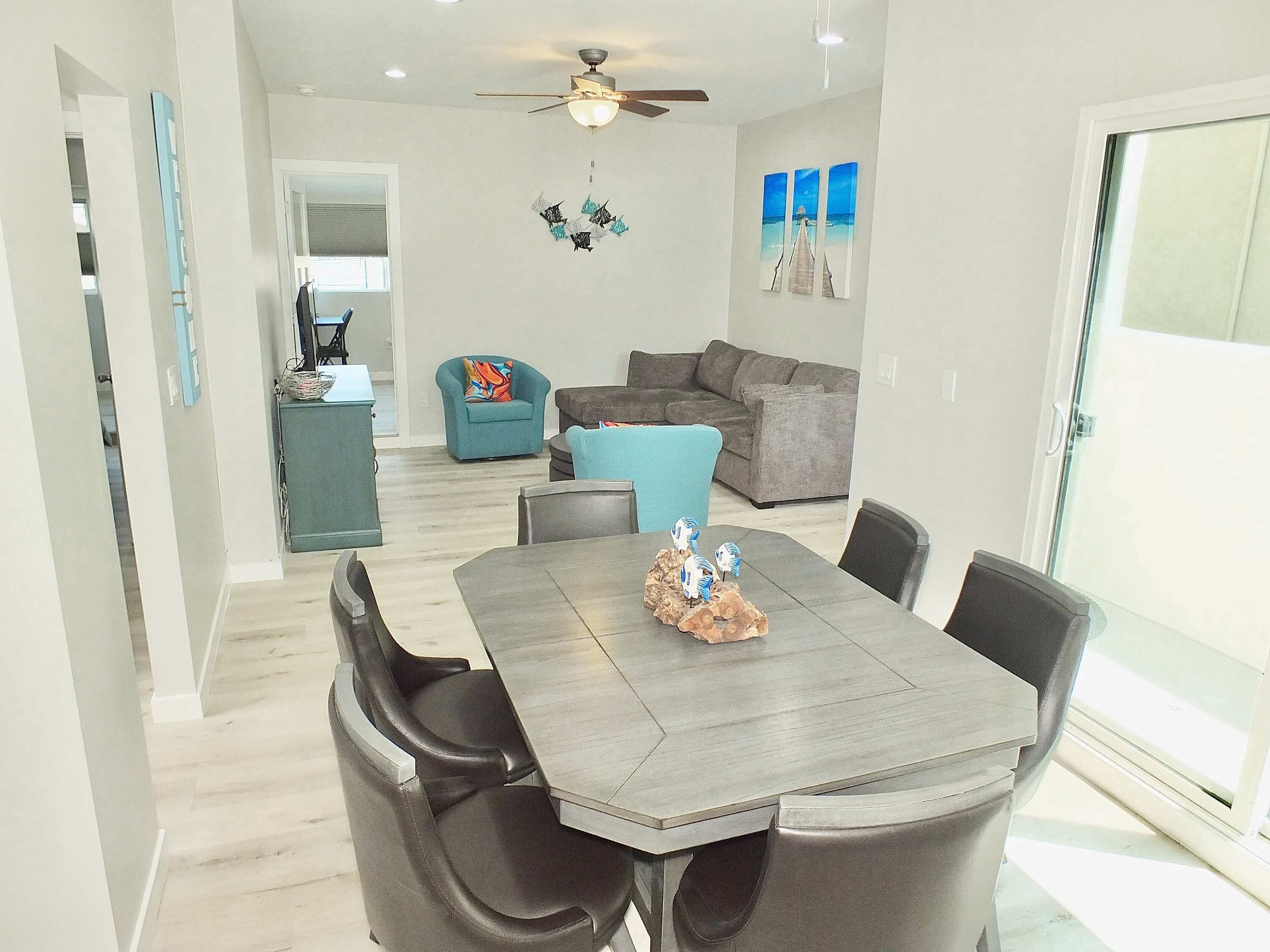 A modern dining area with a grey table and black chairs, a grey sofa, and a teal armchair.