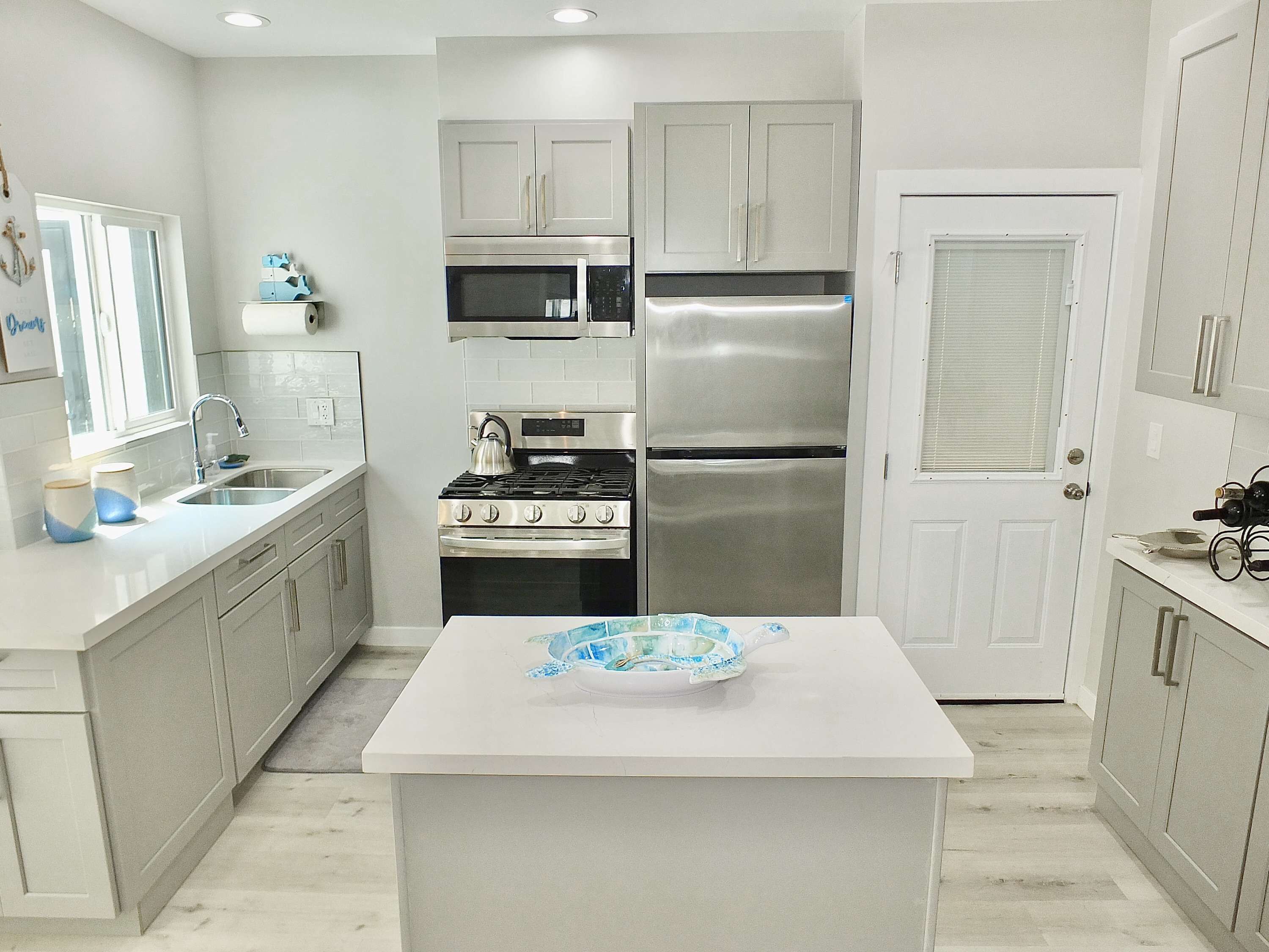 A modern kitchen with white cabinets, stainless steel appliances, a central island, and a window providing natural light.