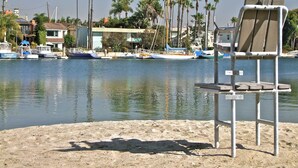 A beach chair on a sandy shore with a calm body of water in the background, surrounded by palm trees and boats. - New Beach & Bay Retreat Full of Amenities! (Long Beach)