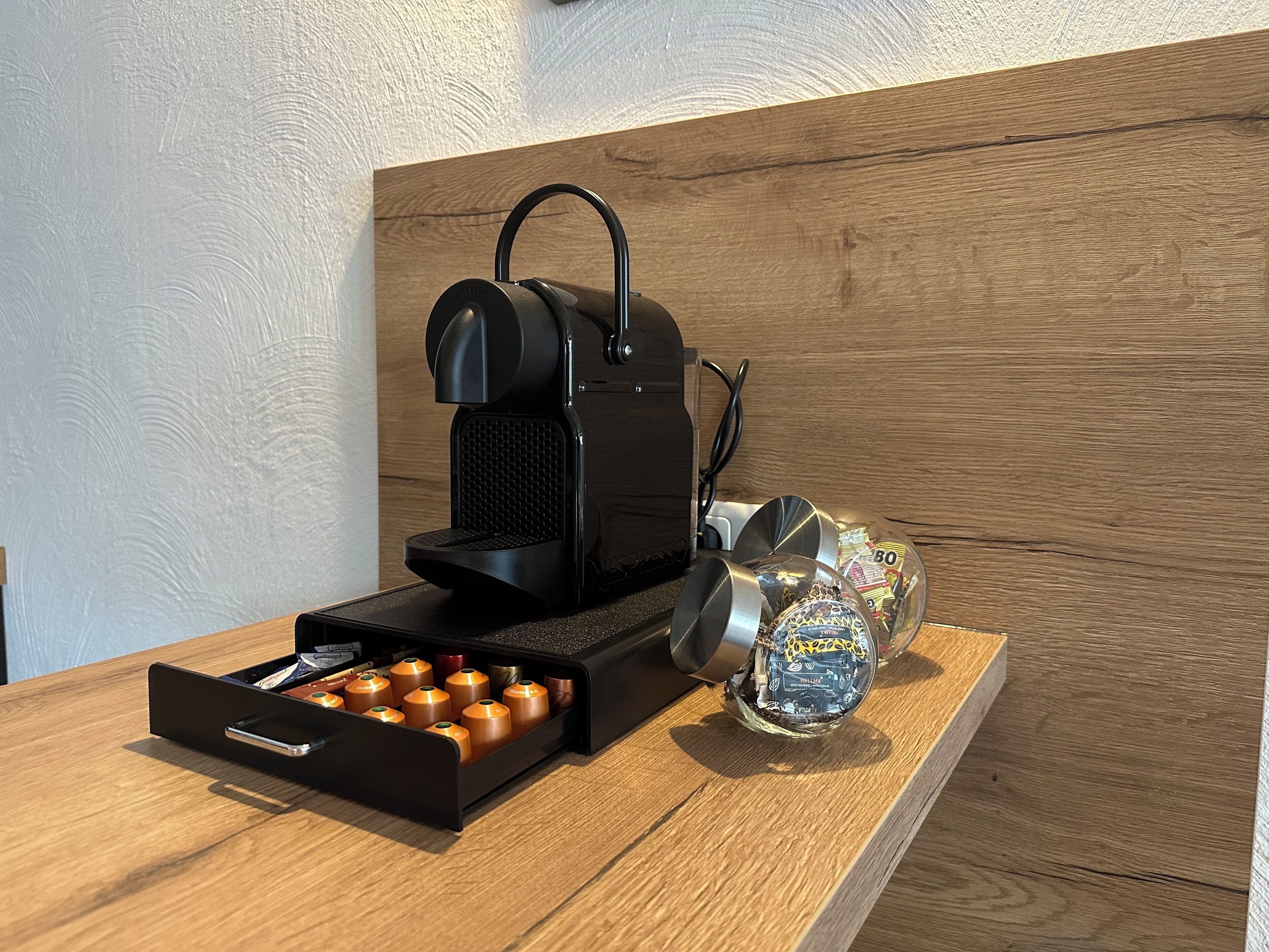 Eine Kaffeemaschine mit Auffangbehälter und Kapselhalter auf einer Holzoberfläche.