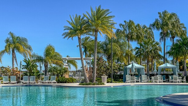 A clear blue pool with lounge chairs and umbrellas, surrounded by palm trees and a gazebo. - Always Summer on Sunshine Ridge (Kissimmee)