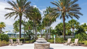 A pathway lined with palm trees and Adirondack chairs, leading to a stone fire pit. - Always Summer on Sunshine Ridge (Kissimmee)