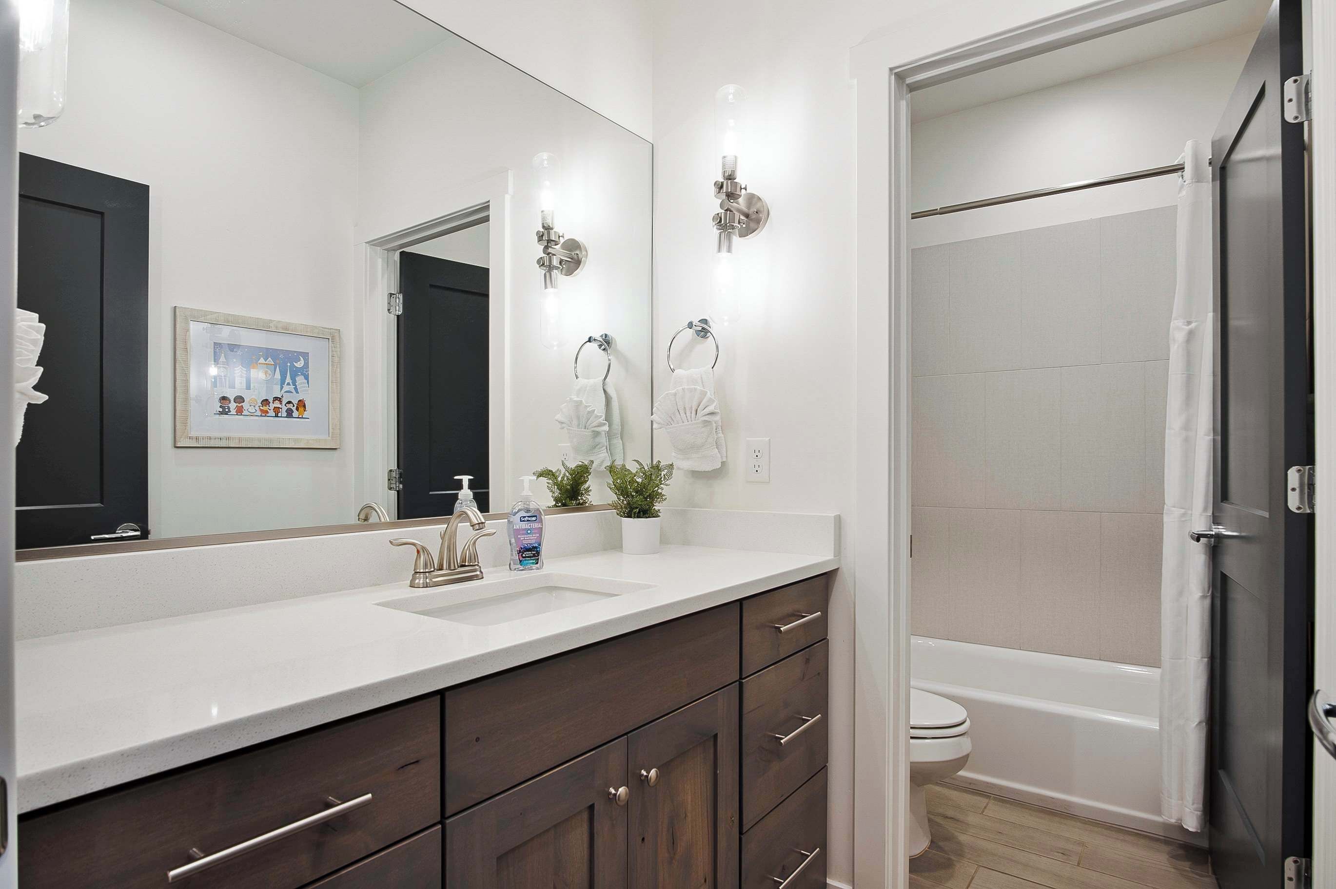 A modern bathroom with a white sink, dark wooden cabinets, a large mirror, a shower with a glass door, and a toilet.