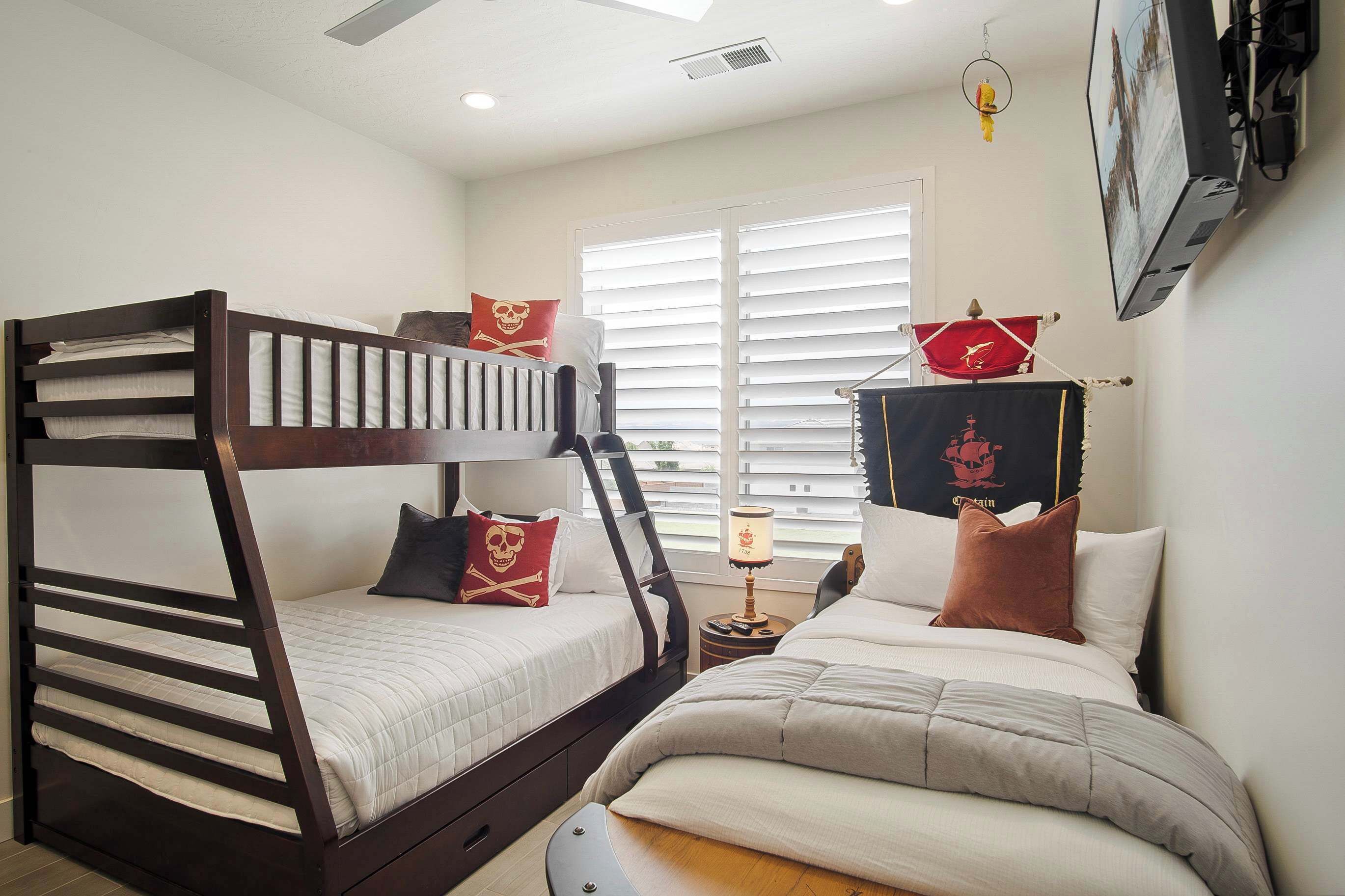 A bedroom with two bunk beds, a window with blinds, a nightstand with a lamp, and a wall-mounted TV.