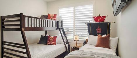A bedroom with two bunk beds, a window with blinds, a nightstand with a lamp, and a wall-mounted TV.