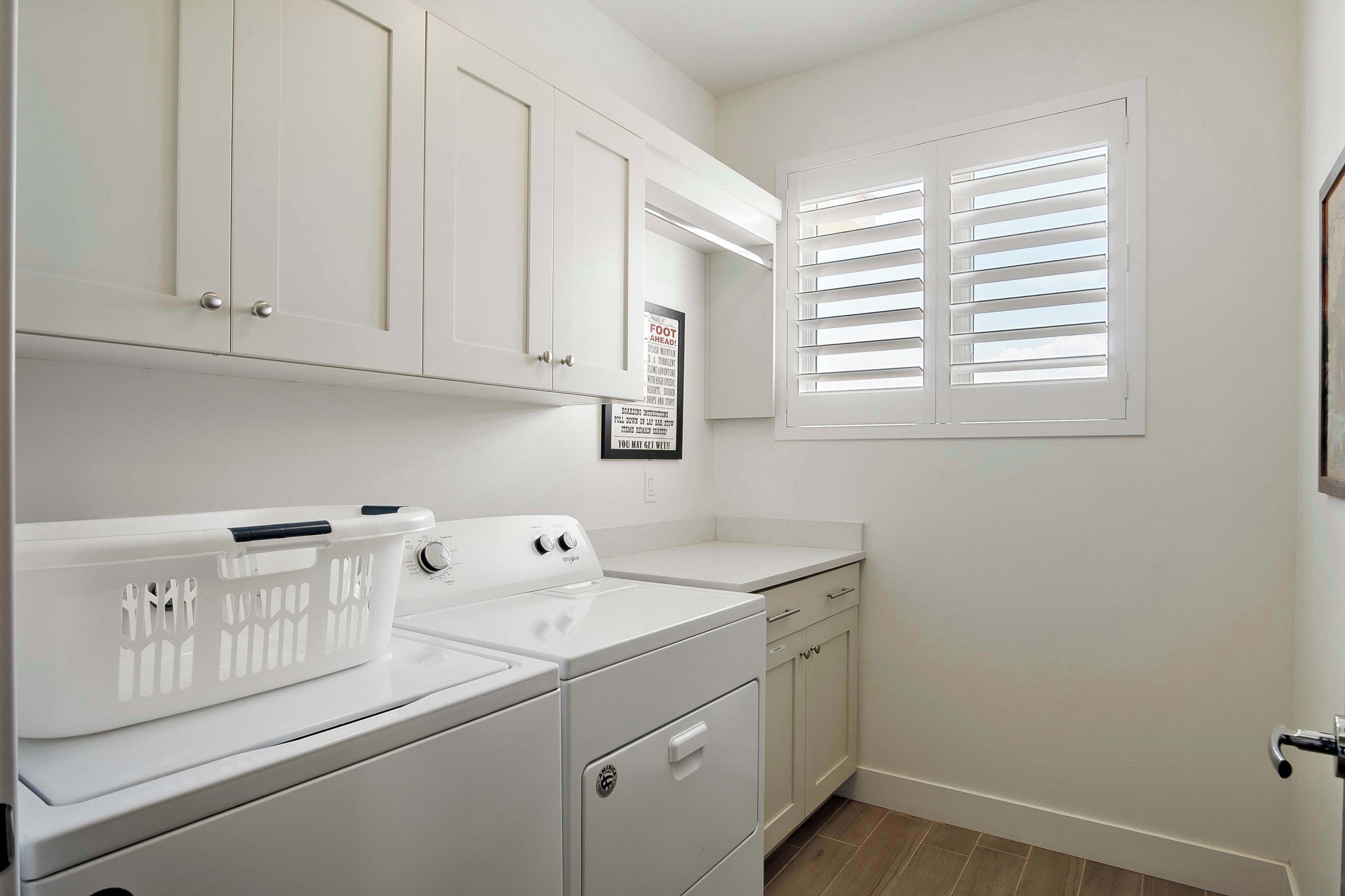 A laundry room with white appliances, a laundry basket, and a window with blinds.