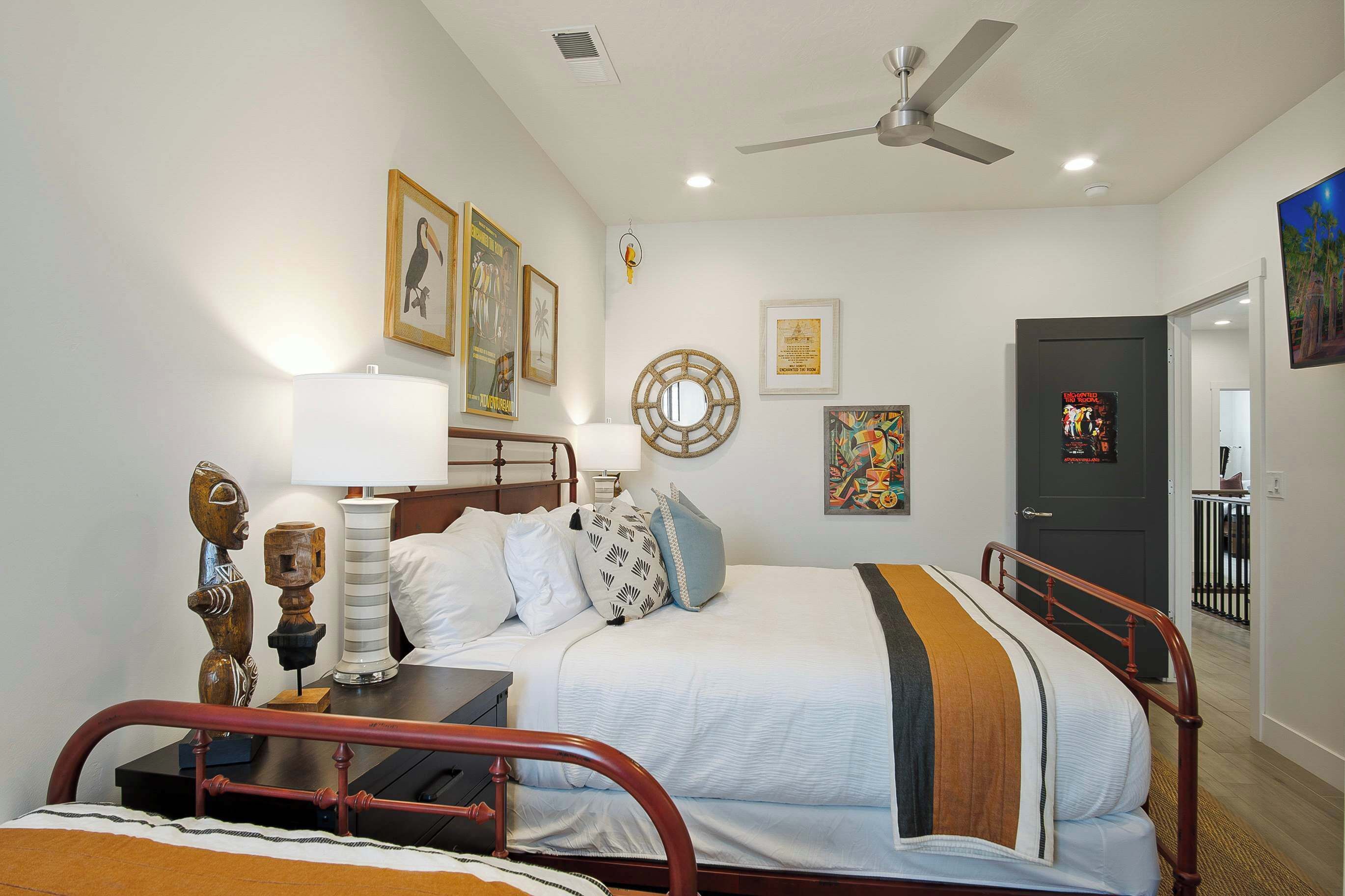 Un dormitorio con cama, mesitas de noche, ventilador de techo y obras de arte en las paredes.