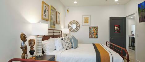 Un dormitorio con cama, mesitas de noche, ventilador de techo y obras de arte en las paredes.
