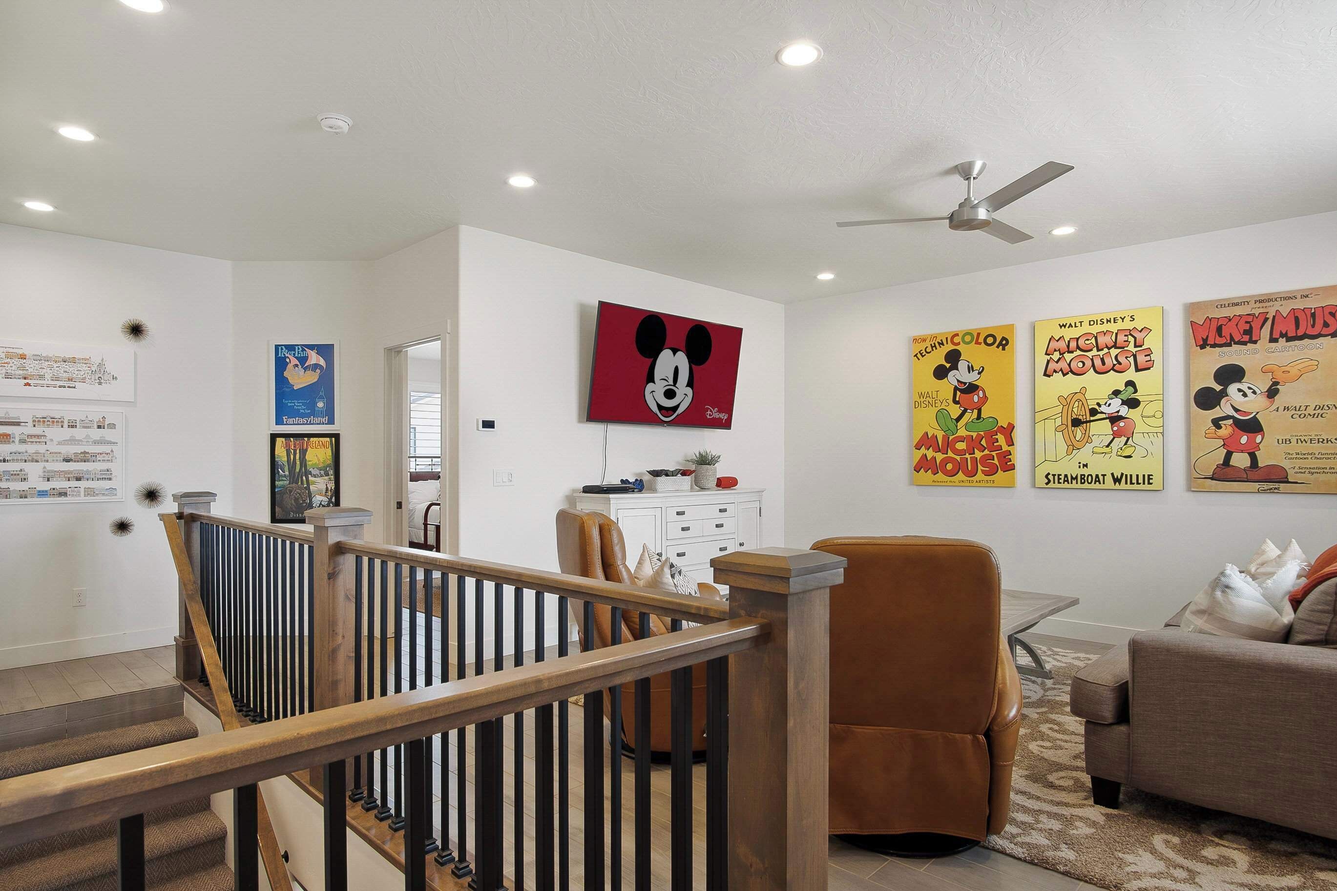Ein Wohnzimmer mit Treppe, Deckenventilator und Postern an der Wand.