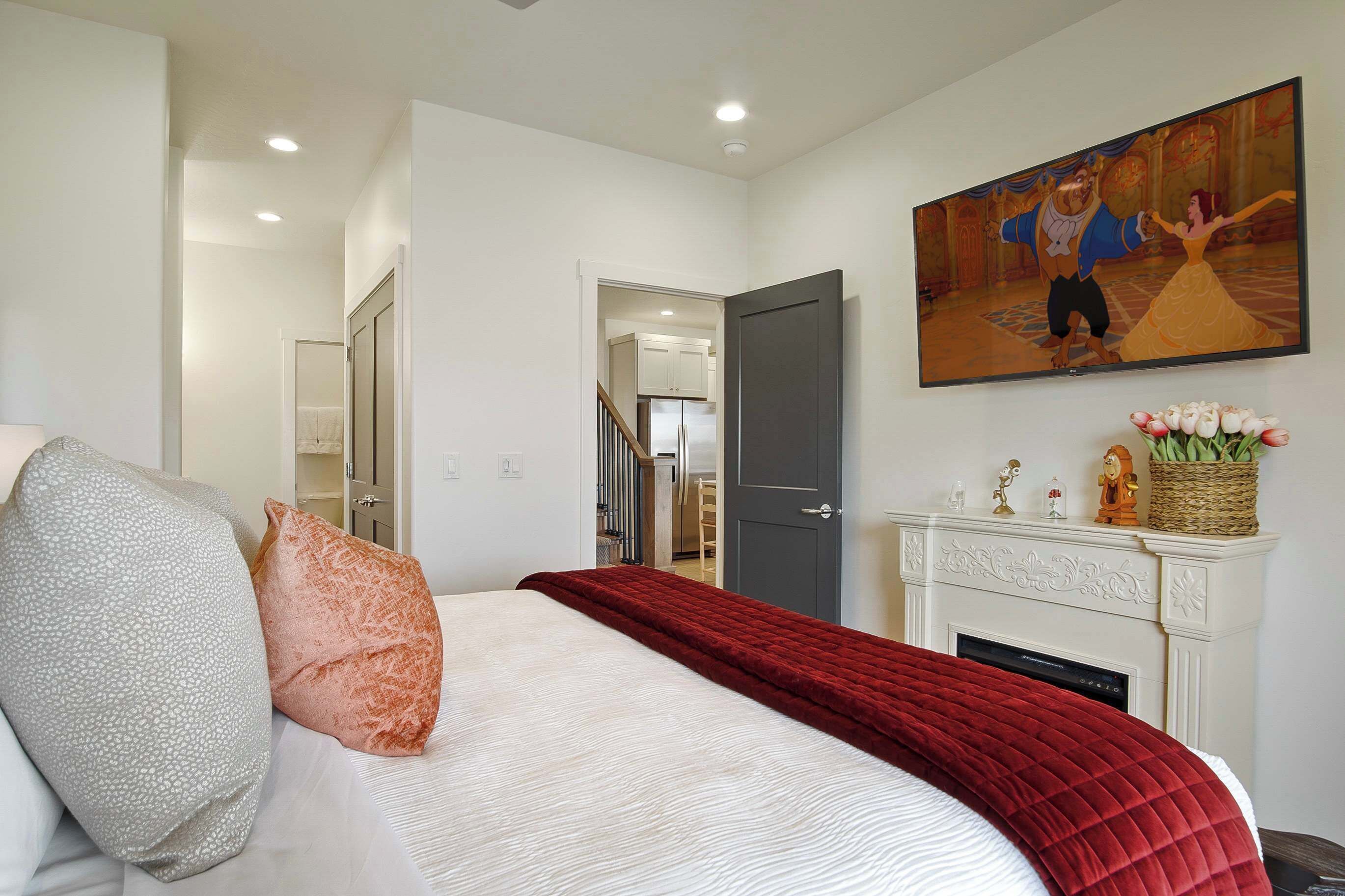 A bedroom with a bed, pillows, a red blanket, a fireplace, and a painting on the wall.