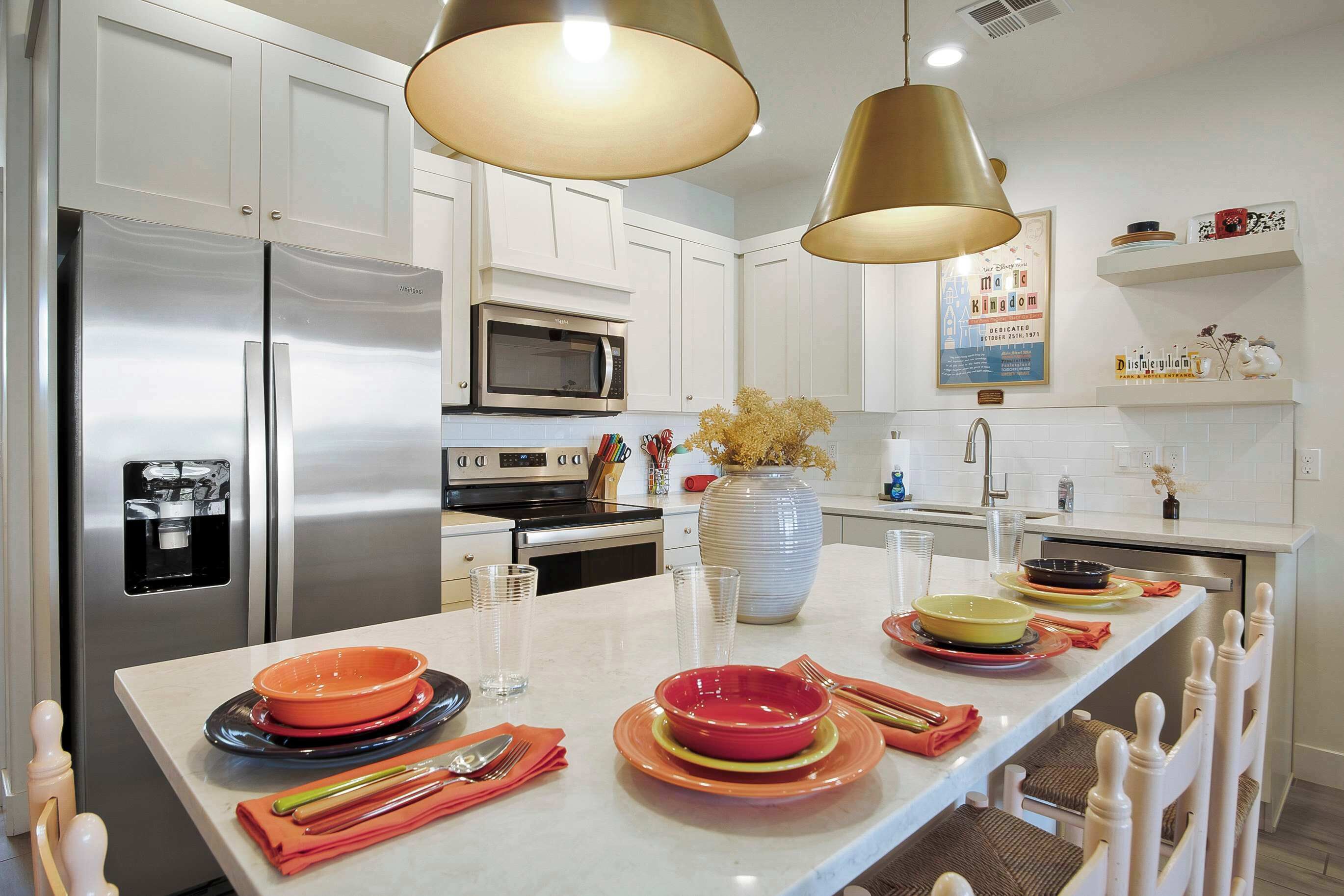 A modern kitchen with stainless steel appliances, a central island with diningware, and pendant lighting.