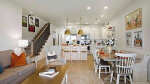 A modern living room with a sofa, coffee table, and a dining area with chairs and a table. A staircase leads to the upper floor. - New Listing Be Our Guest in Utah (Washington)