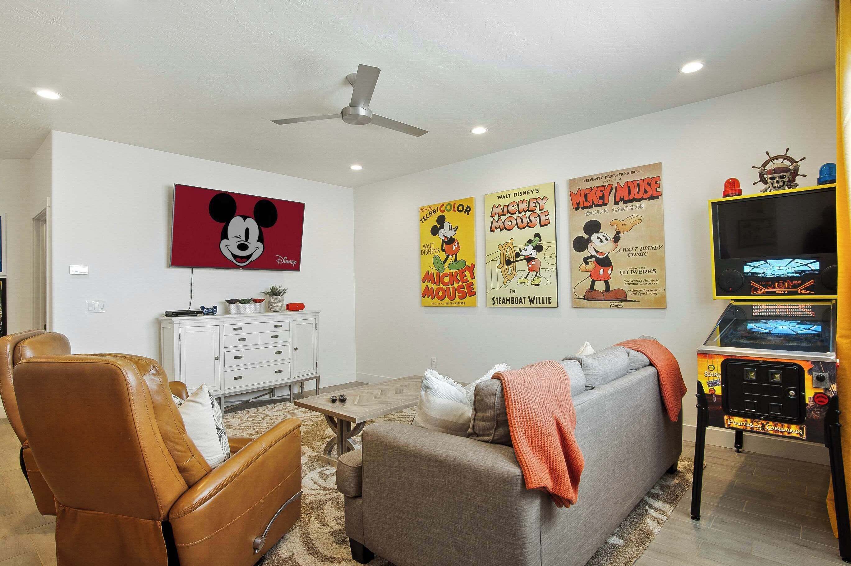 A living room with a television, posters, a gaming console, and a ceiling fan.