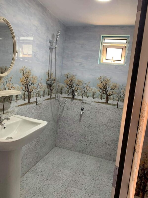 Een badkamer met een wastafel, douche en een klein raam.