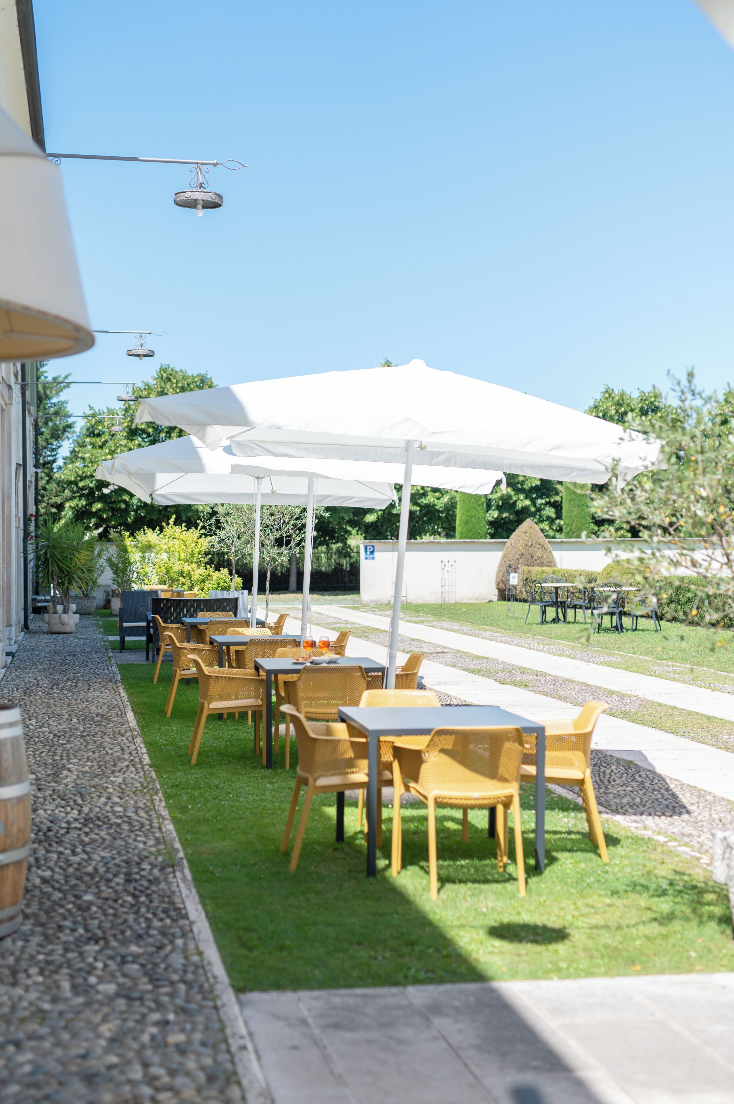 An outdoor seating area with tables and chairs under white umbrellas, a gravel path, and a well-maintained lawn.