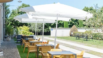 An outdoor seating area with tables and chairs under white umbrellas, a gravel path, and a well-maintained lawn.