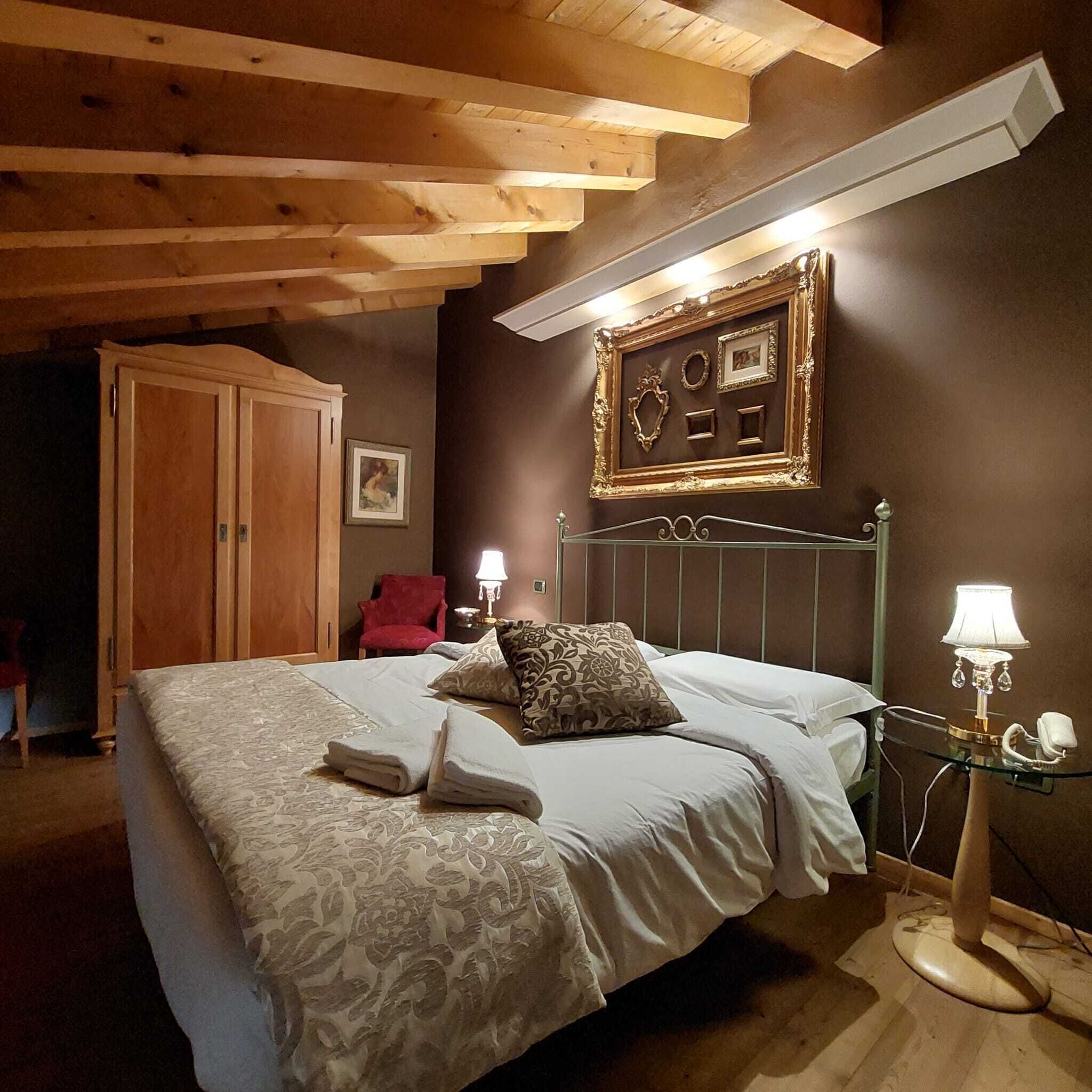 A bedroom with a bed, a wardrobe, a red chair, a bedside table with a lamp, and a wall-mounted picture frame.