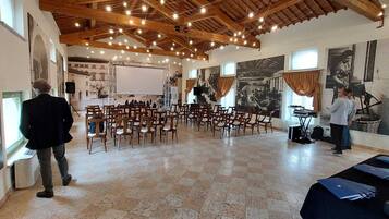 Un salón amplio con techo alto y vigas de madera, que cuenta con un escenario con instrumentos musicales y sillas dispuestas para el público.