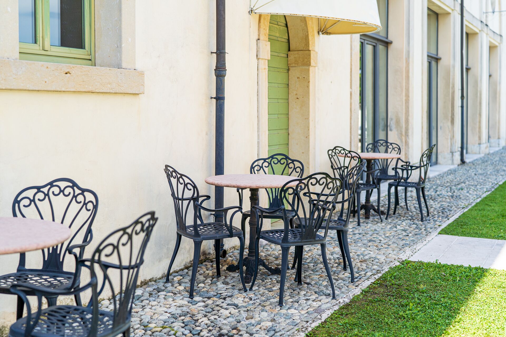 Outdoor seating with tables and chairs, a green door, and a building facade.