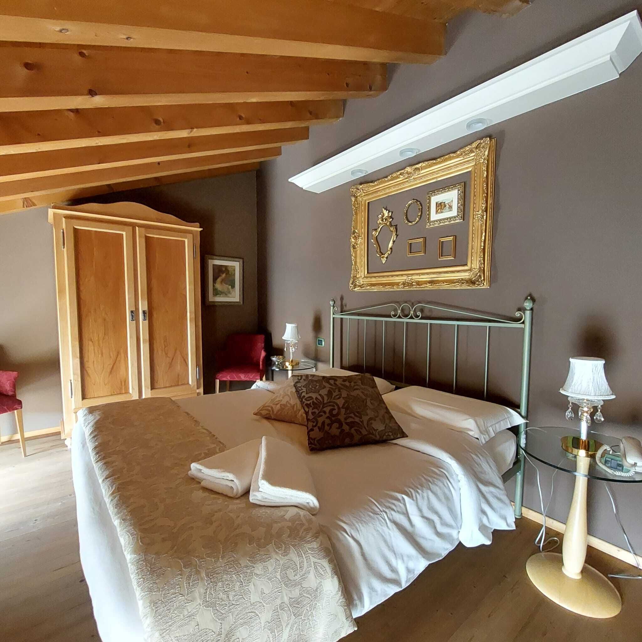 A bedroom with a bed, a wardrobe, a red chair, a bedside table with a lamp, and a wall with framed pictures.