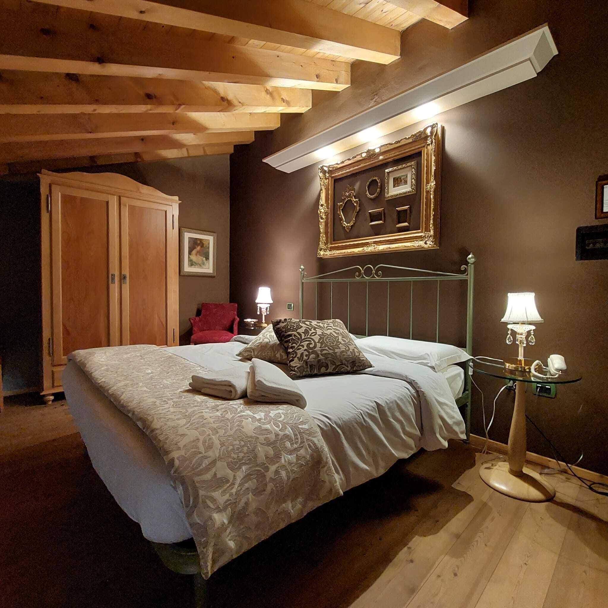 A bedroom with a bed, bedside lamps, a wooden wardrobe, and a framed picture on the wall.