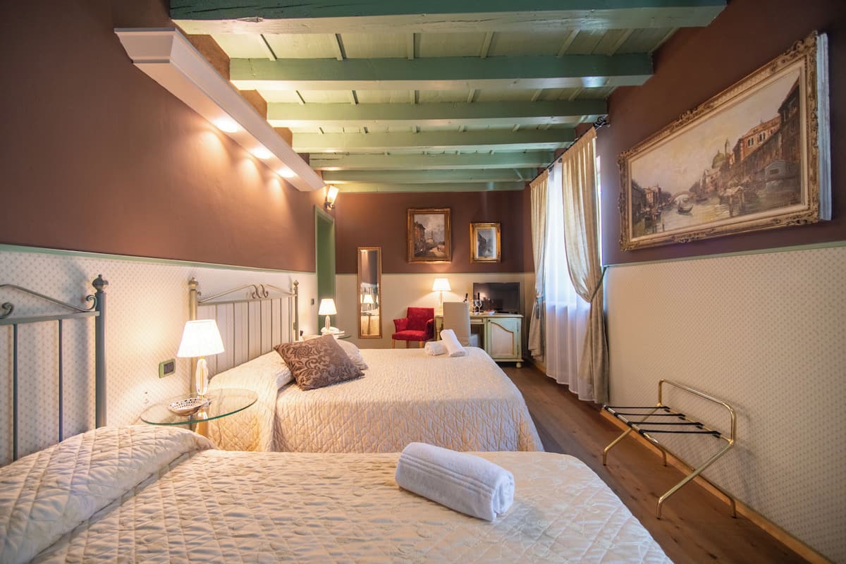 Habitación de hotel con dos camas, un escritorio, una silla y un cuadro en la pared.