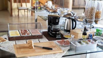 A breakfast buffet with various food items, a coffee machine, and a bottle of red wine.