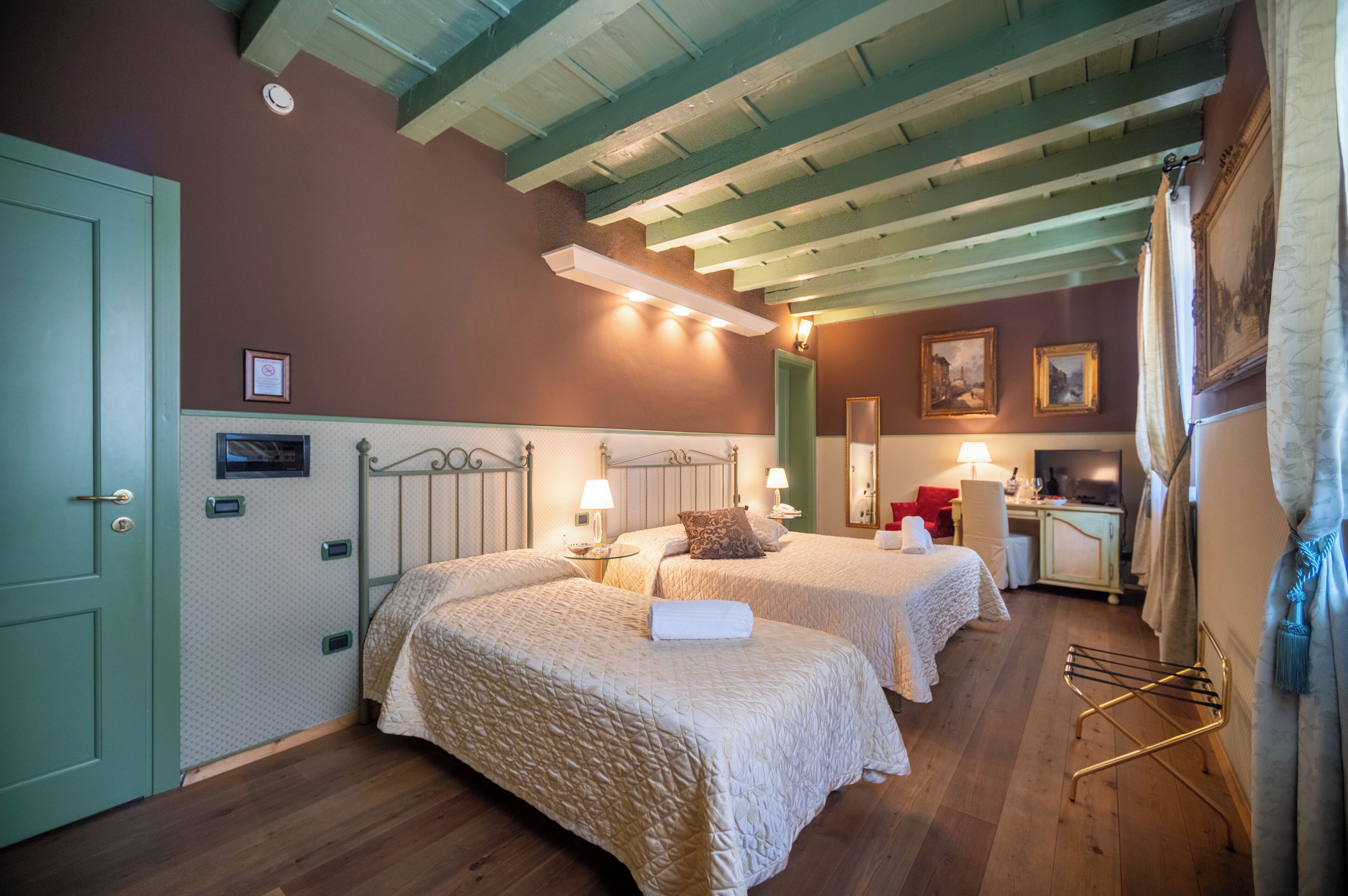 A room with two beds, a small desk, and a mirror. There is a door on the left and a window on the right.