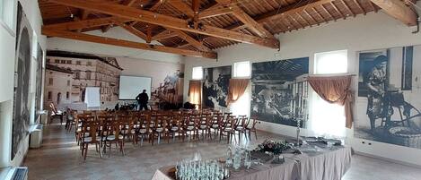 A spacious hall with high wooden ceilings, rows of chairs, and a stage with a projector.