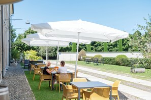 An outdoor patio with tables and chairs under white umbrellas, surrounded by greenery and a clear sky. - Residenza Villa Vecelli (Mozzecane)