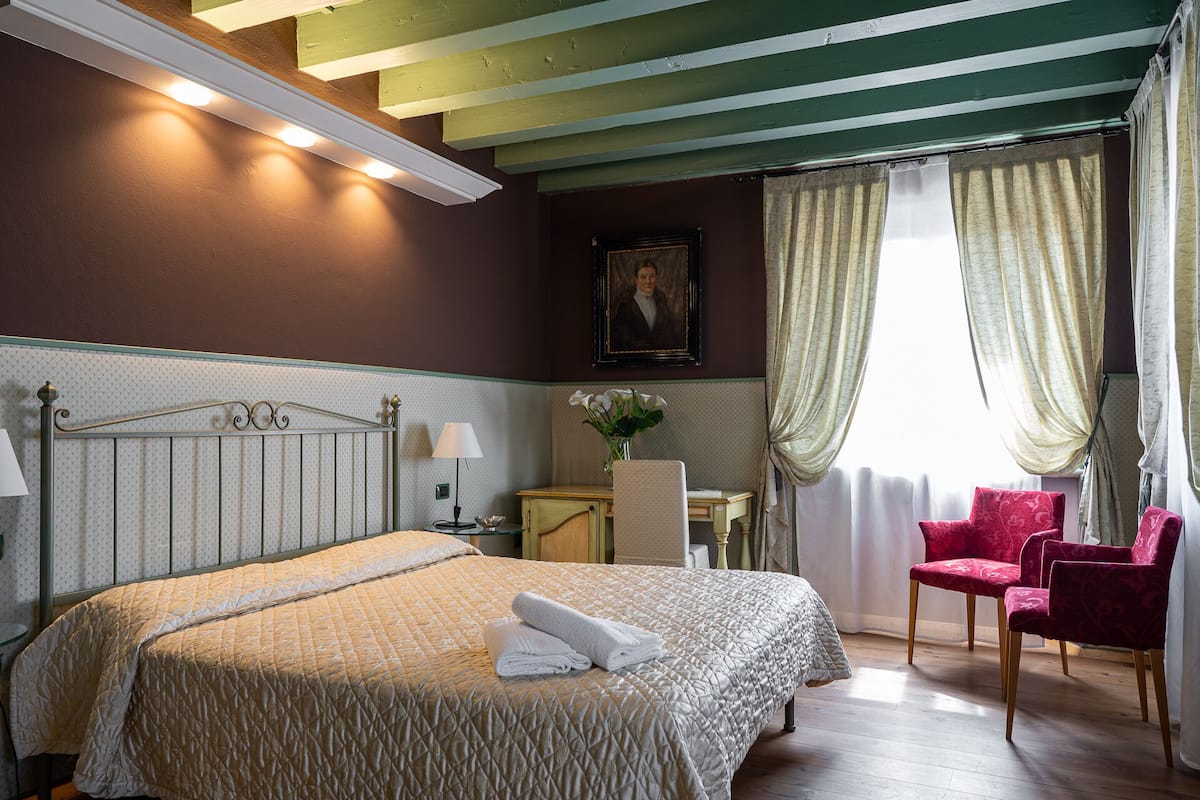 Una habitación de hotel con cama, escritorio, silla y ventana con cortinas.