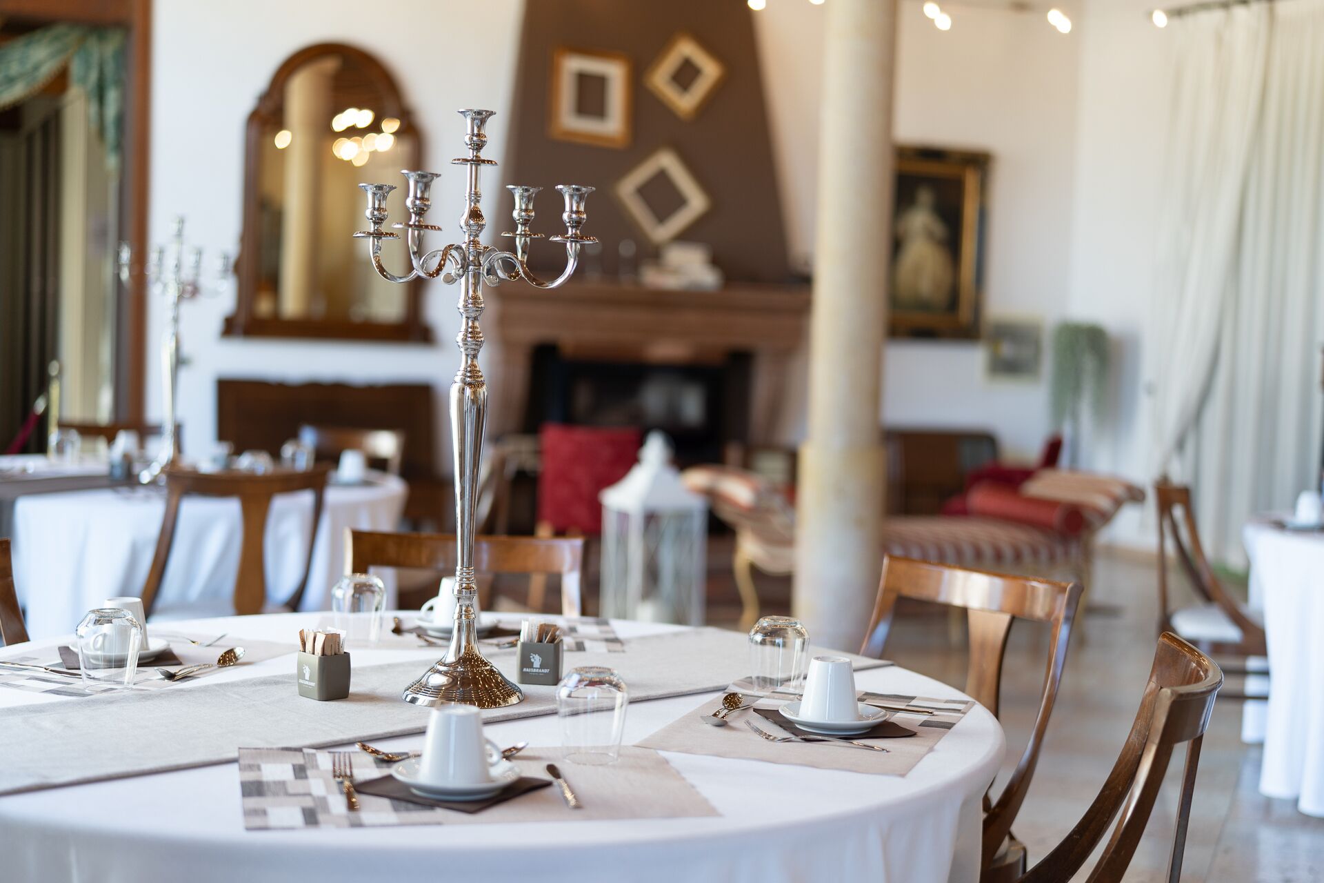A dining area with round tables set for a meal, featuring white tablecloths, silverware, and glassware.