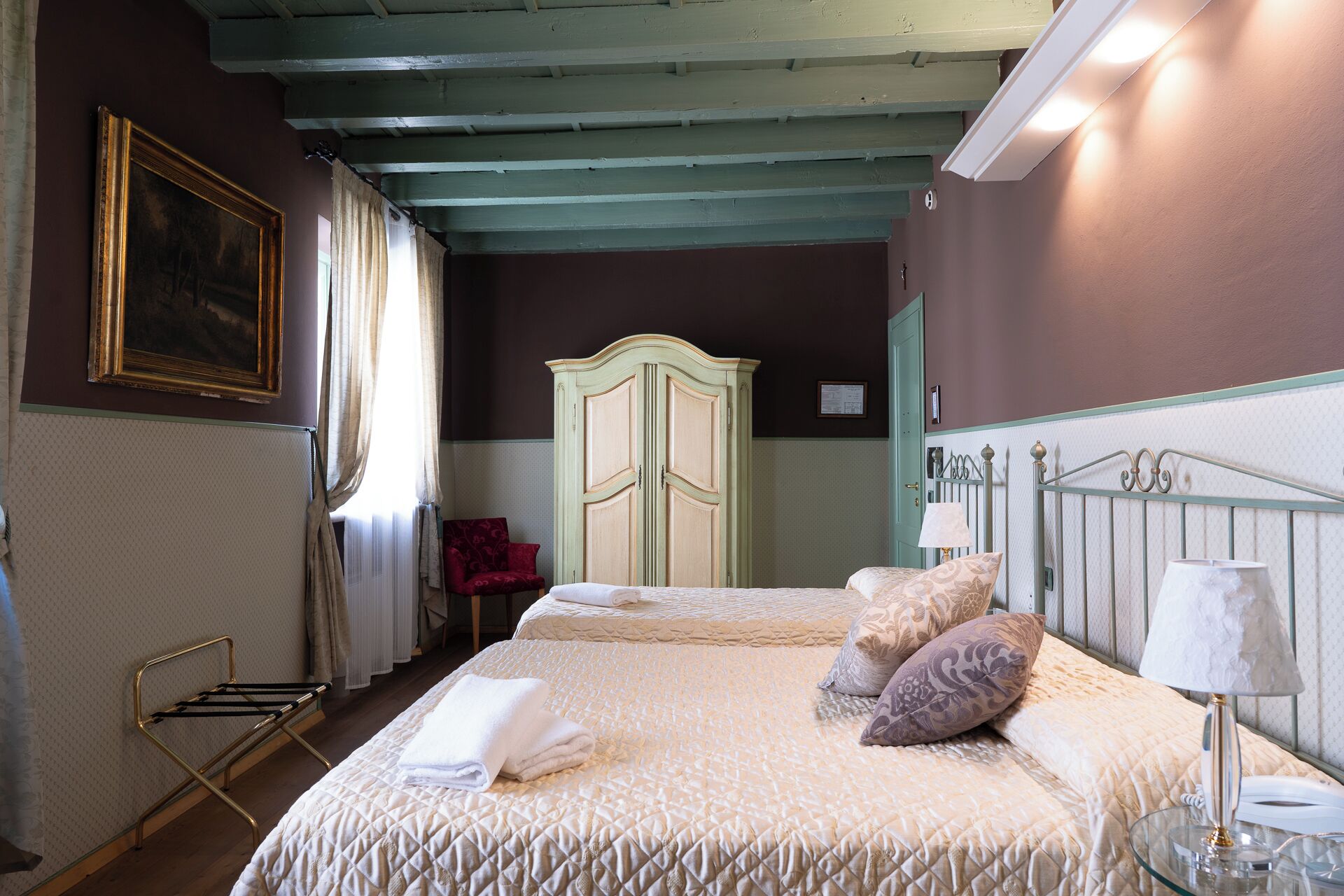 A bedroom with a bed, a wardrobe, a chair, and a painting on the wall.