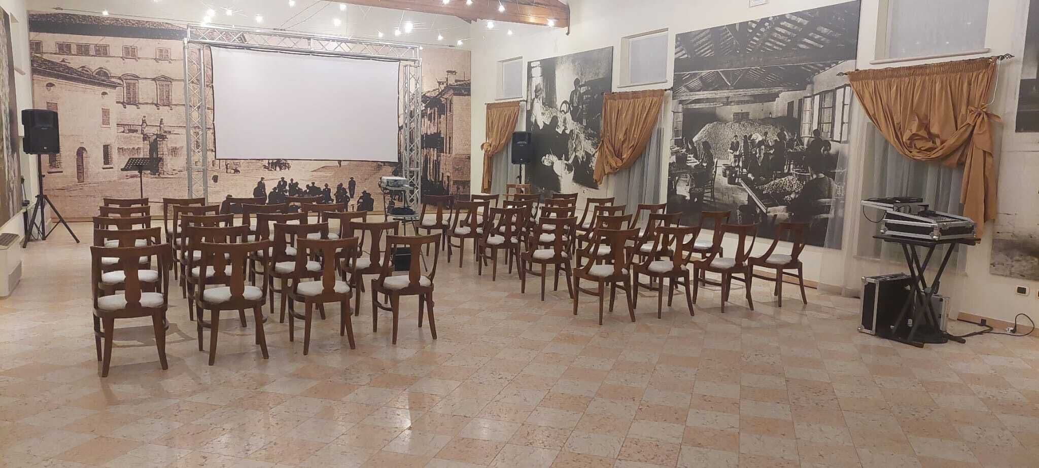 Ein Konferenzraum mit Reihen aus Holzstühlen, einer großen Projektionsleinwand und Vintage-Fotos an den Wänden.