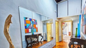 Una habitación amplia con suelo de parquet de madera, un espejo grande que refleja la habitación, y un cuadro abstracto de colores en la pared.