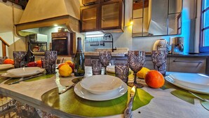 Una cocina bien iluminada con electrodomésticos modernos, un comedor con una mesa larga dispuesta para una comida, y vista al área de estar a través de un arco abierto.