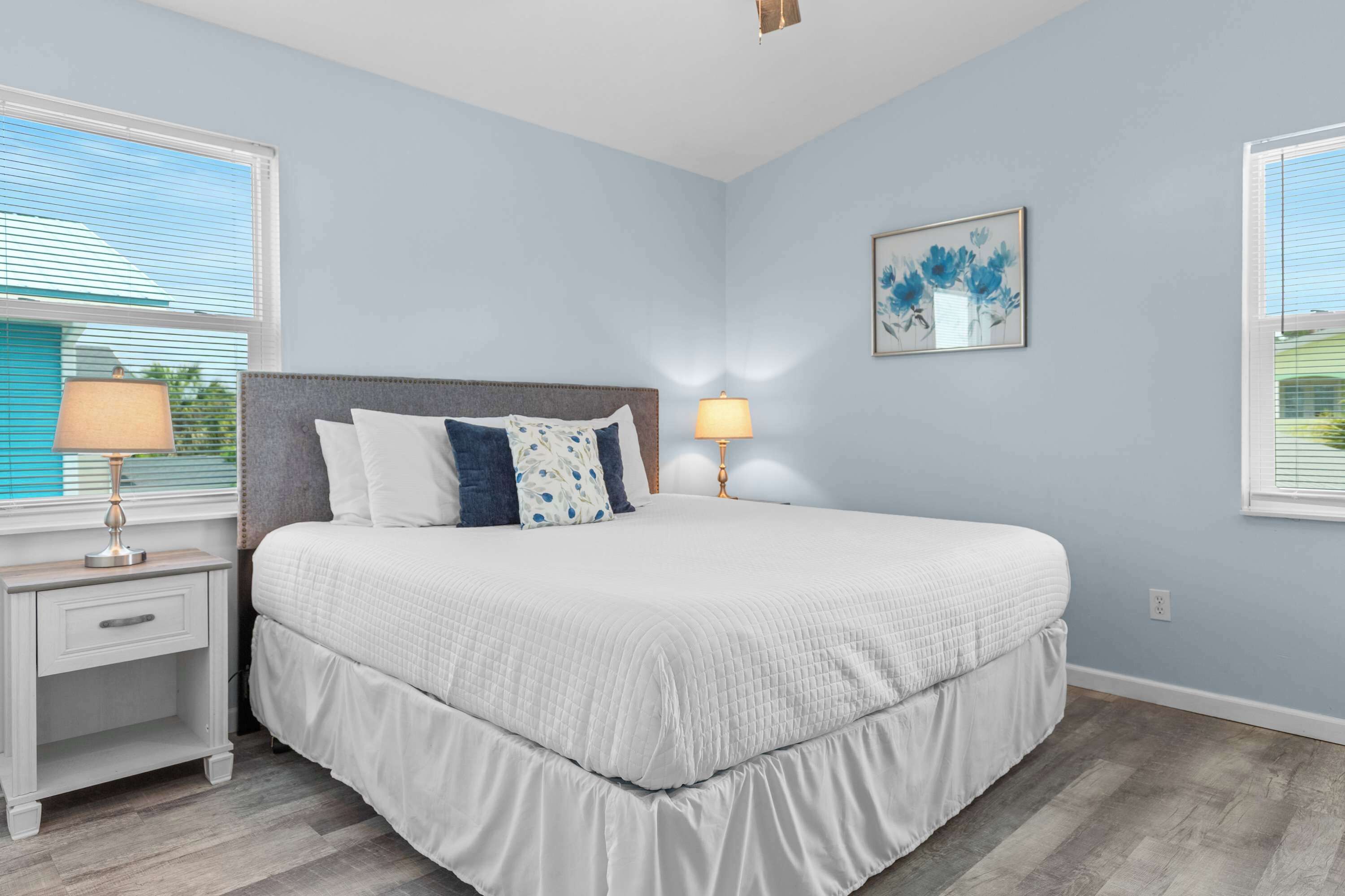 A bedroom with a bed, nightstands, lamps, and a wall-mounted artwork.
