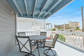 A covered outdoor area with a table and chairs, a white lattice partition, and a view of buildings in the background. - Beach Time Cozy Retreat Steps From the Gulf (Panama City Beach)