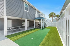 A residential backyard with artificial turf, a wooden deck, and a staircase leading to a second floor.