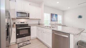 A modern kitchen with white cabinets, stainless steel appliances, a granite countertop, and a dishwasher. - Beach Getaway Community Amenities! (Panama City Beach)