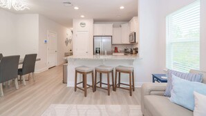 A modern kitchen with white cabinets, a stainless steel refrigerator, and a bar stool area. - Beach Getaway Community Amenities! (Panama City Beach)