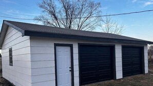 Een laag gebouw met een witte gevel en een donker dak. Het heeft een voordeur en twee garagepoorten.