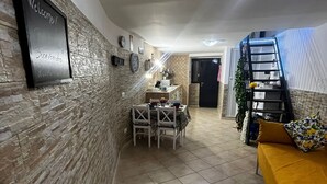 A spacious living area with a tiled floor, a dining table with chairs, a sofa, a staircase, and a wall-mounted air conditioning unit. - In the heart of Naples. Pets allowed. Stroller and crib available free of charge. (Napoli)
