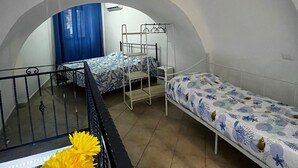 A dormitory room with three bunk beds, a small table with a yellow flower, and a staircase leading to an upper level. - In the heart of Naples. Pets allowed. Stroller and crib available free of charge. (Napoli)