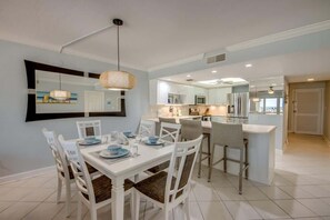 A modern kitchen with white cabinetry, a dining area with a white table and chairs, and a large mirror above the dining table.