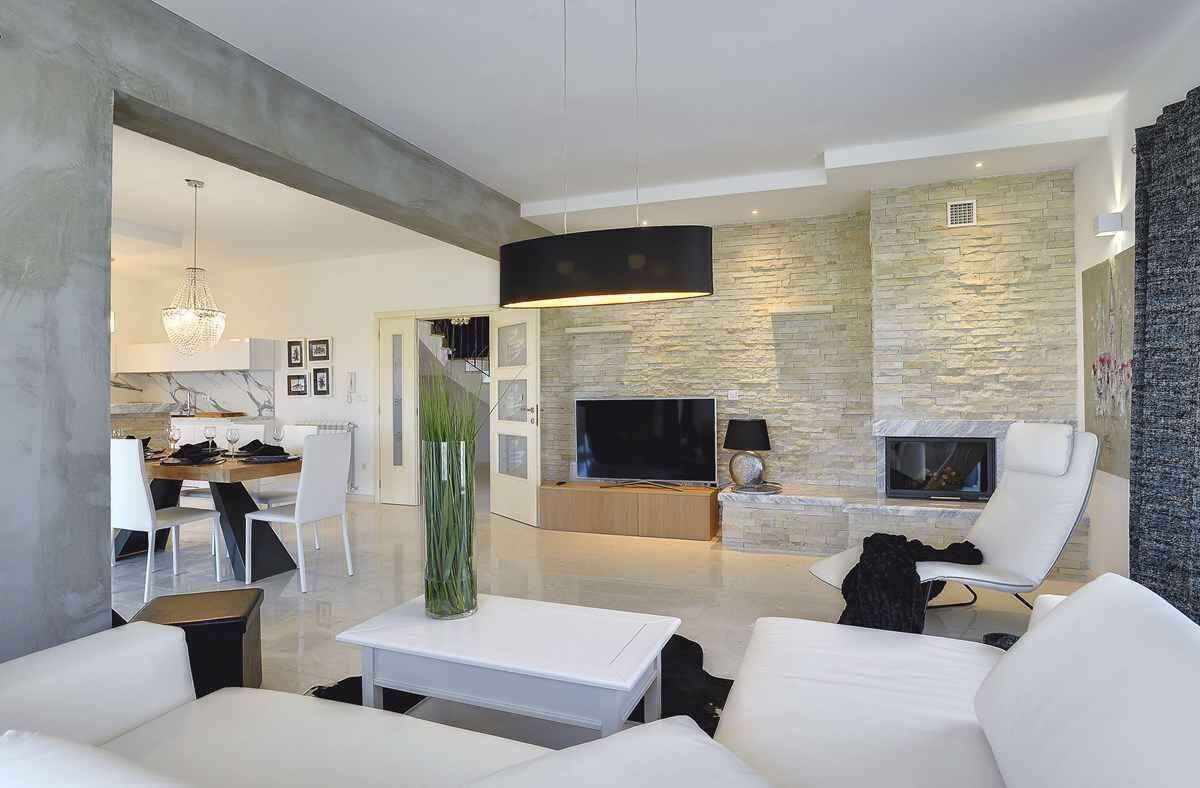 A modern living room with a stone accent wall, a flat-screen TV, and a fireplace.