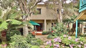 Een huis met een tuin, een terras met een tafel en stoelen, en een overdekt gebied met een groene parasol.