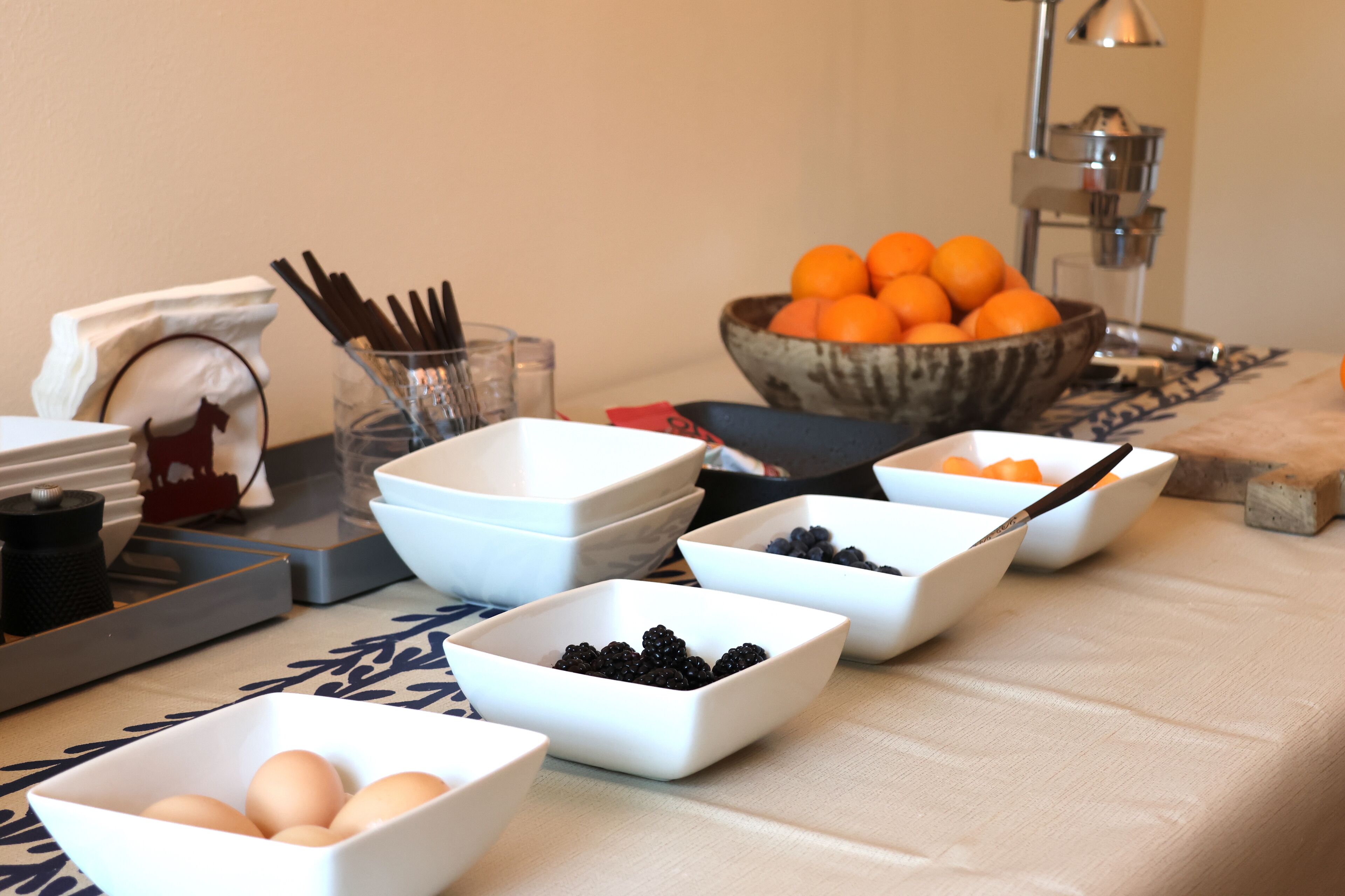 A breakfast buffet with various food items in bowls, including eggs, blackberries, and oranges.