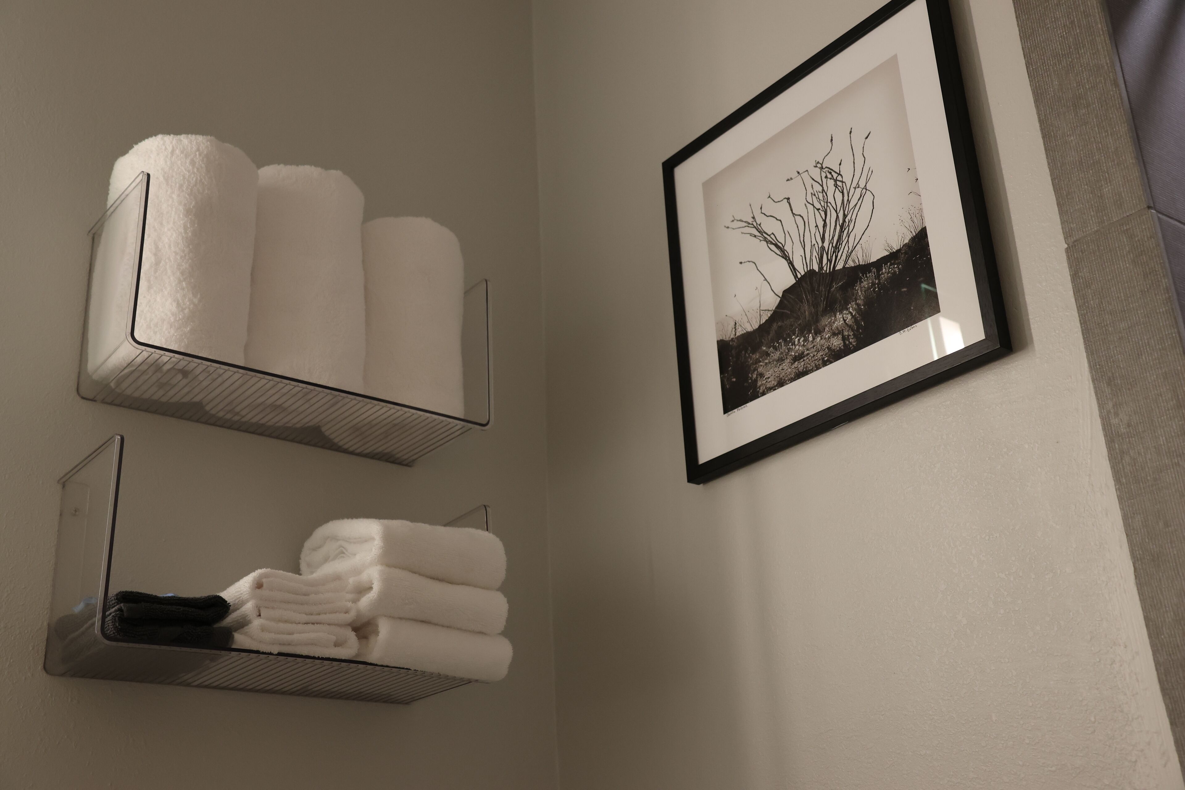 A bathroom with two towel racks, one holding white towels and the other holding black towels. A framed black and white photograph is on the wall.
